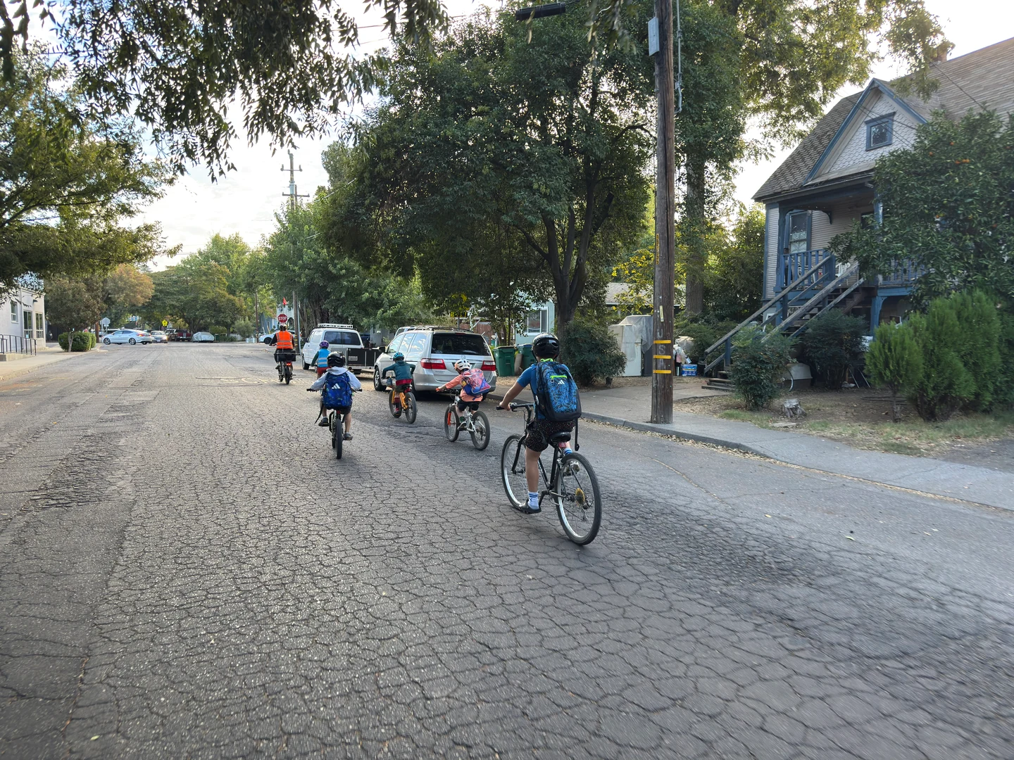 The bike group riding along a neighborhood street past houses and parked cars